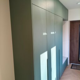 Pracownia Meblowa Modena - Długa, oliwkowa szafa wnękowa z siedziskiem, w przedpokoju z parkietem ułożonym w jodełkę. Minimalistyczny design, brak uchwytów, drzwi sięgają sufitu.