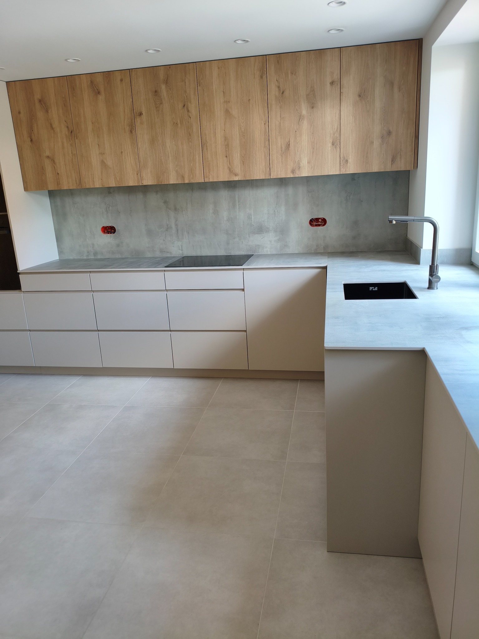 Nowoczesna kuchnia z drewnianymi szafkami górnymi i jasnymi dolnymi. Minimalistyczny design, szara ściana i blat. Bateria kuchenna po prawej stronie, widok z góry na zlew.