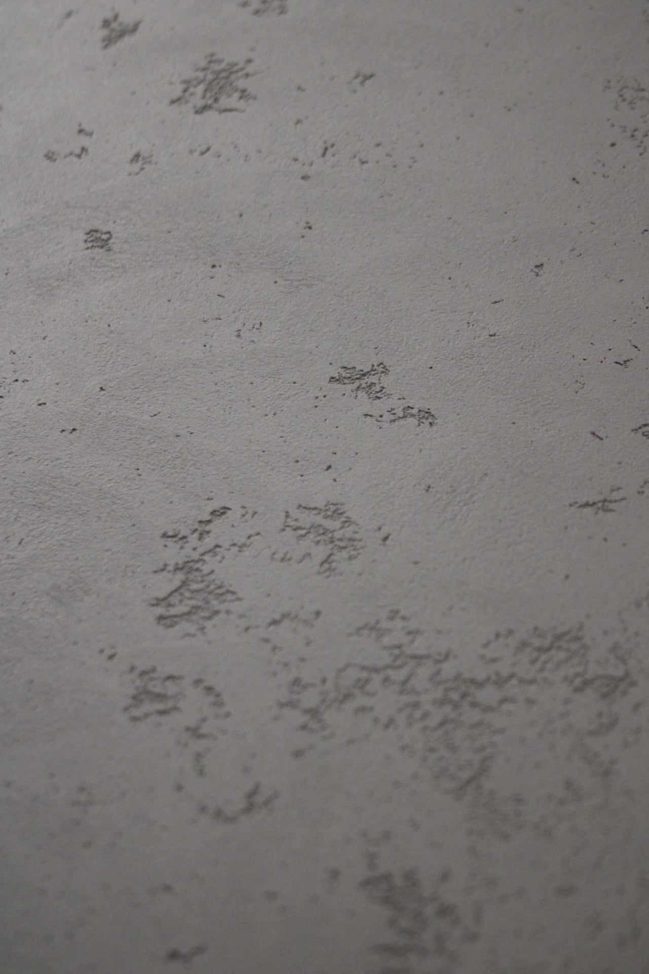 Szara, teksturowana ściana z widocznymi nierównościami i delikatnymi wzorami, imitująca beton architektoniczny w zbliżeniu.