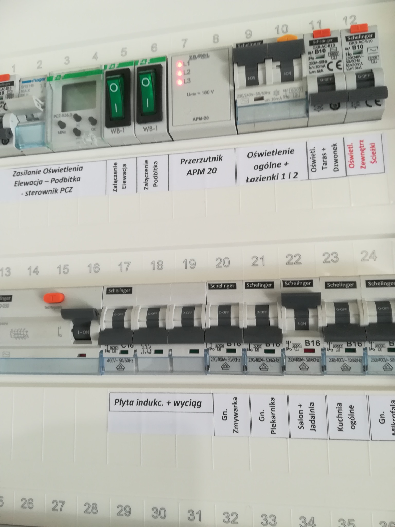 Rozdzielnica elektryczna z opisami obwodów, widoczne wyłączniki nadprądowe i różnicowoprądowe, sterownik oświetlenia elewacji i podbitki, oraz przełącznik APM-20, etykiety wskazują obwody dla płyty...