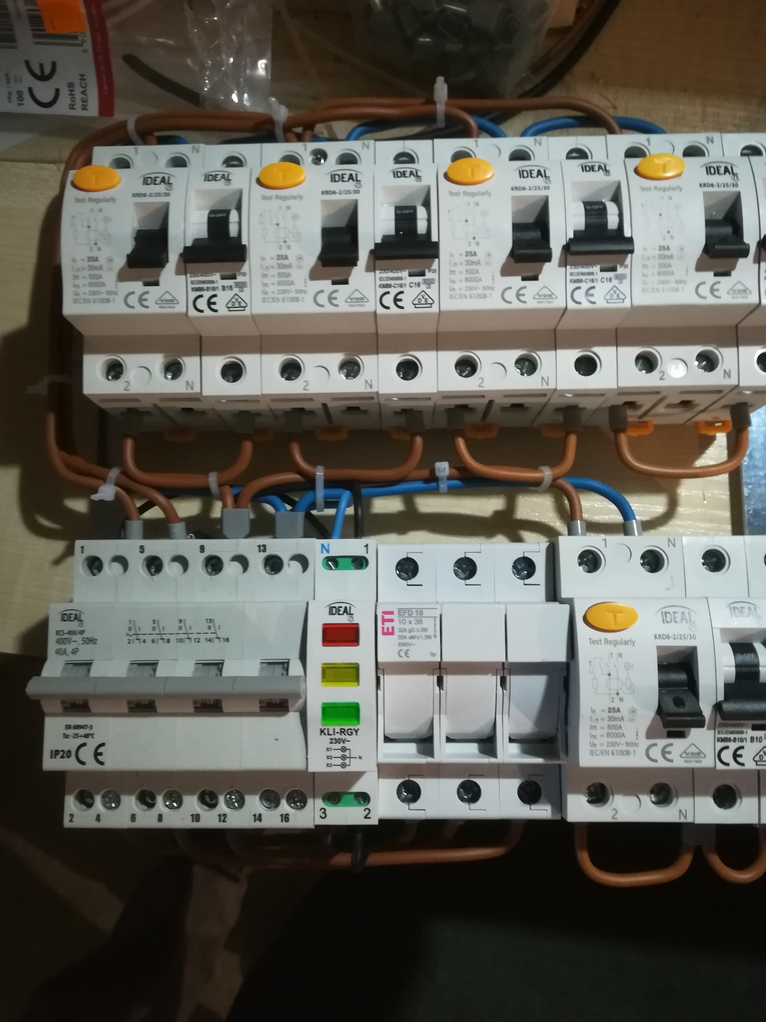 Rozdzielnica elektryczna z zamontowanymi bezpiecznikami i przewodami, widoczne brązowe i niebieskie przewody podłączone do bezpieczników IDEAL KRD6-2/25/30, z żółtymi przyciskami testowymi.