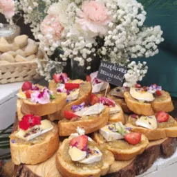 Dekoracyjne kanapeczki z serem brie, truskawkami i kwiatami na drewnianej desce, z napisem 'Szczęśliwych Brzuszków' w tle, przygotowane w Rzeszowie.