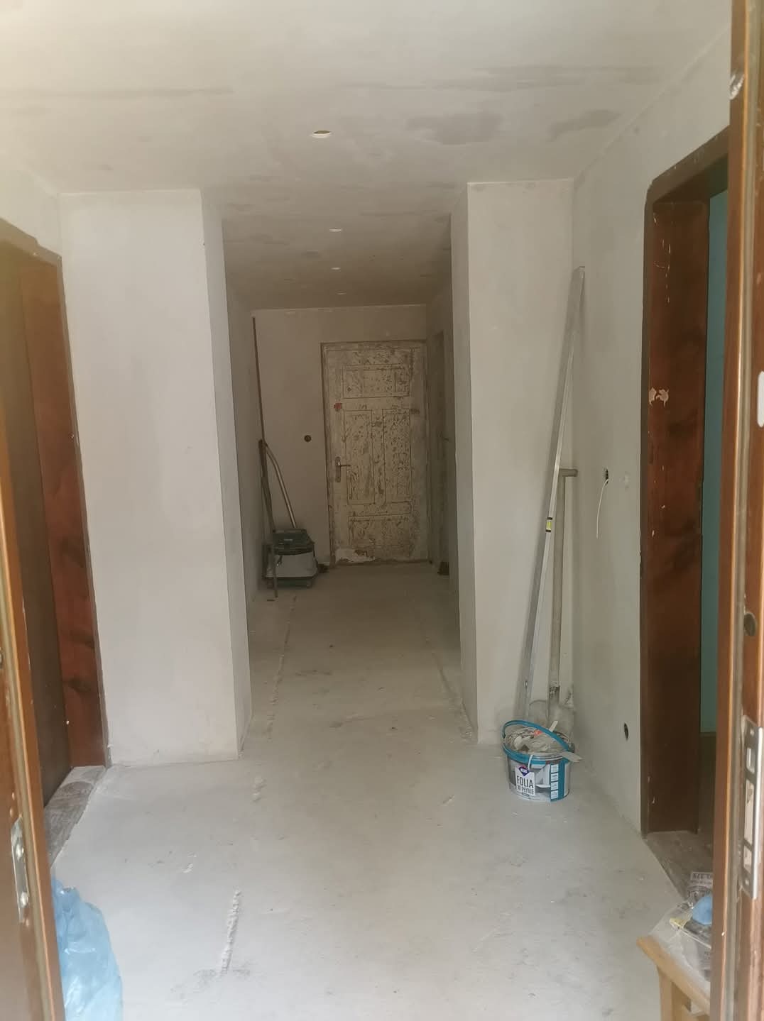 Korytarz w trakcie remontu w Leżajsku: ściany po gładzi, widoczne narzędzia (szpachelka, drabina) i wiadro z farbą Folia, przygotowane do malowania.