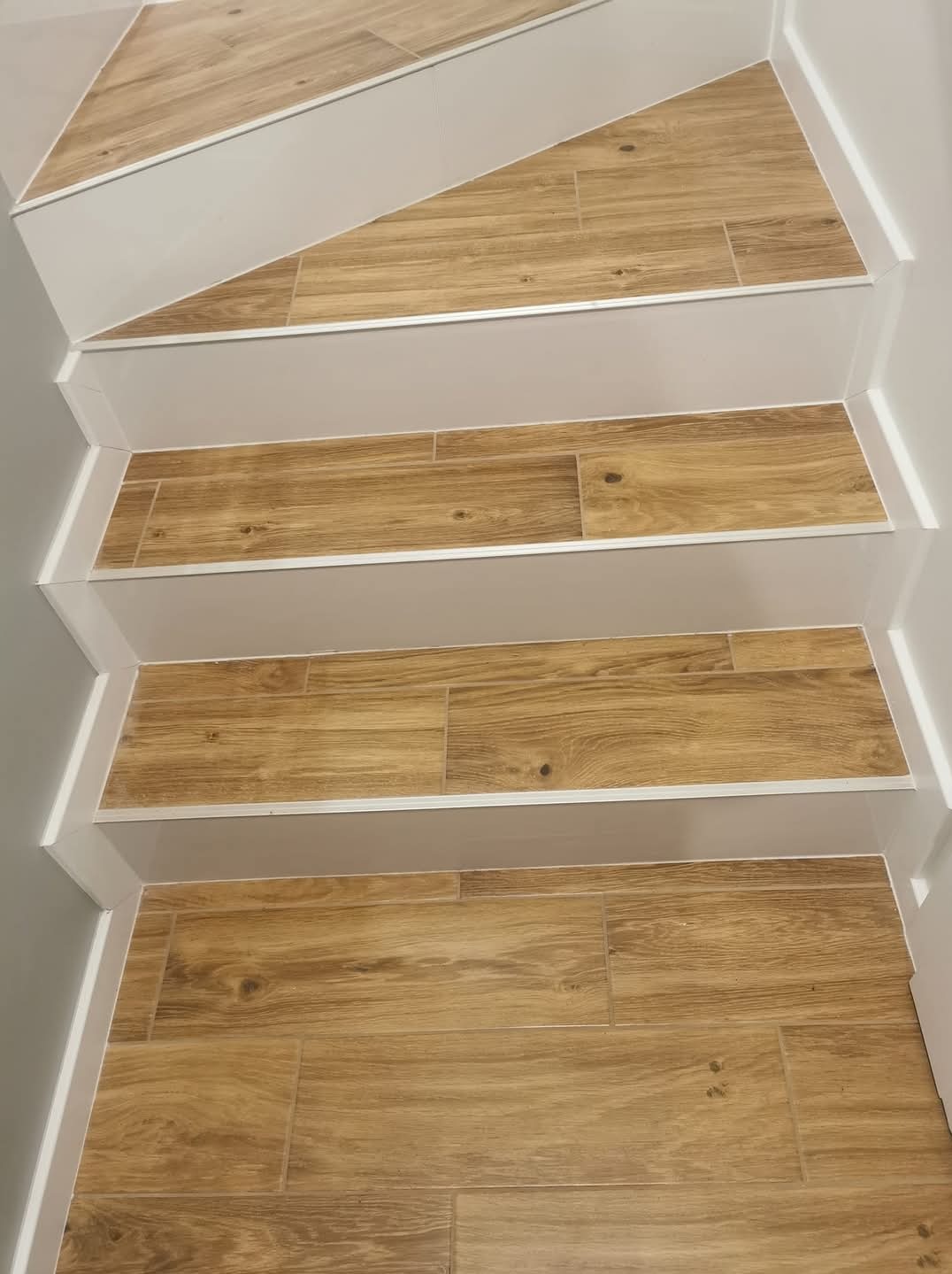 Schody wyłożone płytkami imitującymi drewno, z białymi listwami wykończeniowymi i szarymi ścianami bocznymi, widok z góry na kilka stopni.