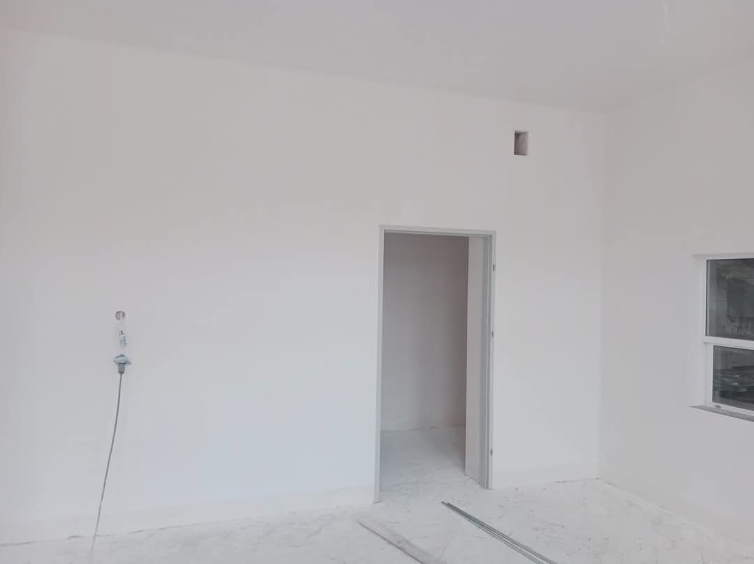 Wnętrze pokoju po malowaniu w Leżajsku, widoczne świeżo pomalowane białe ściany, okno, puste gniazdko elektryczne oraz metalowe listwy na podłodze.