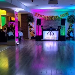 Adimat Mariusz Nowicki - Sala studniówkowa w Bydgoszczy z dekoracjami balonowymi w kolorach czarnym, białym i złotym, oświetleniem LED w odcieniach różu, zieleni i niebieskiego oraz stanowiskiem DJ-a z napisem 'DJ Mario...