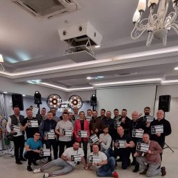 Adimat Mariusz Nowicki - Grupa osób pozuje z dyplomami na tle sceny oświetlonej reflektorami, w tle widoczny napis 'Uwolnij swój potencjał'.