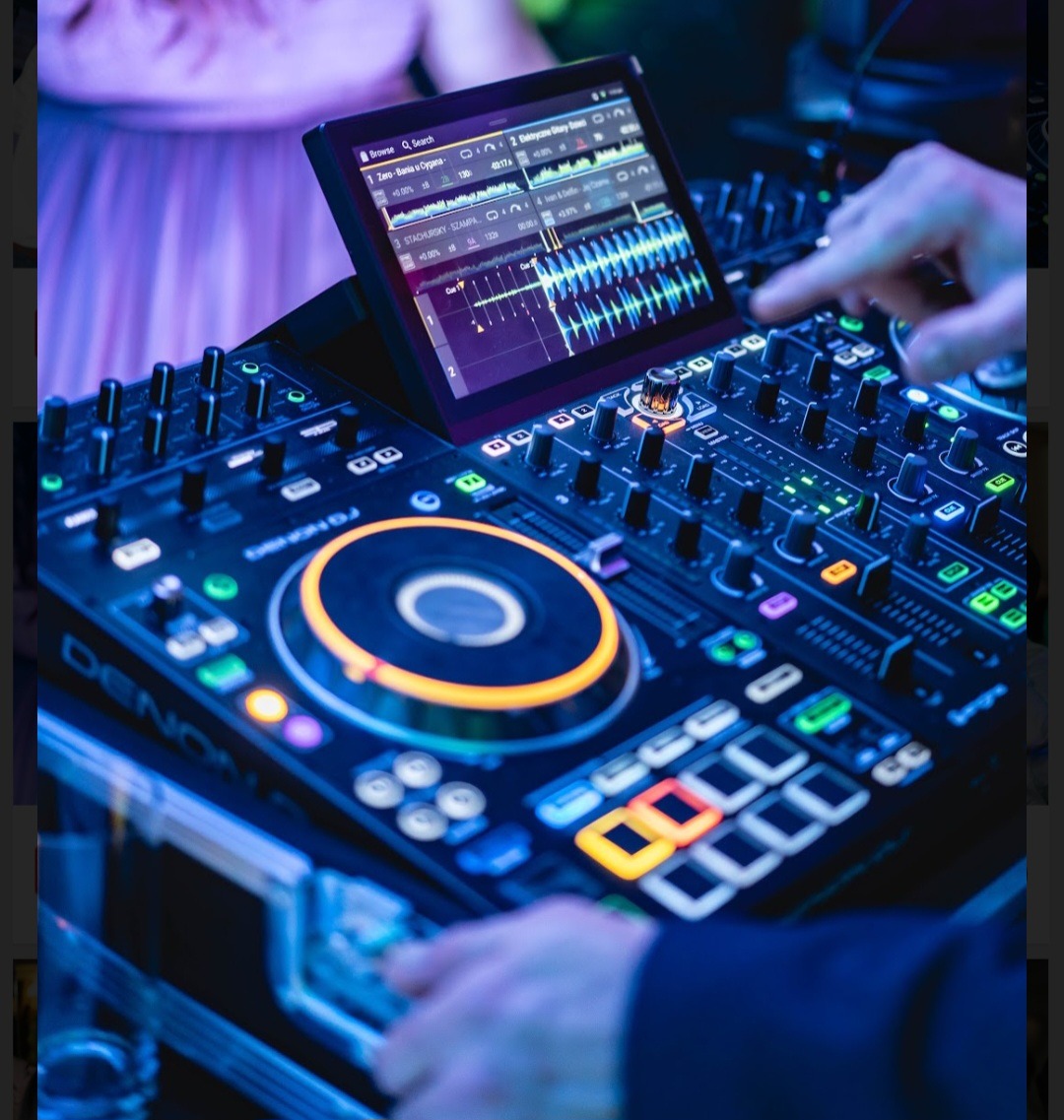 DJ miksuje muzykę na profesjonalnym sprzęcie Denon DJ, na ekranie tabletu widoczne wykresy fal dźwiękowych, w tle fragment sukienki osoby.