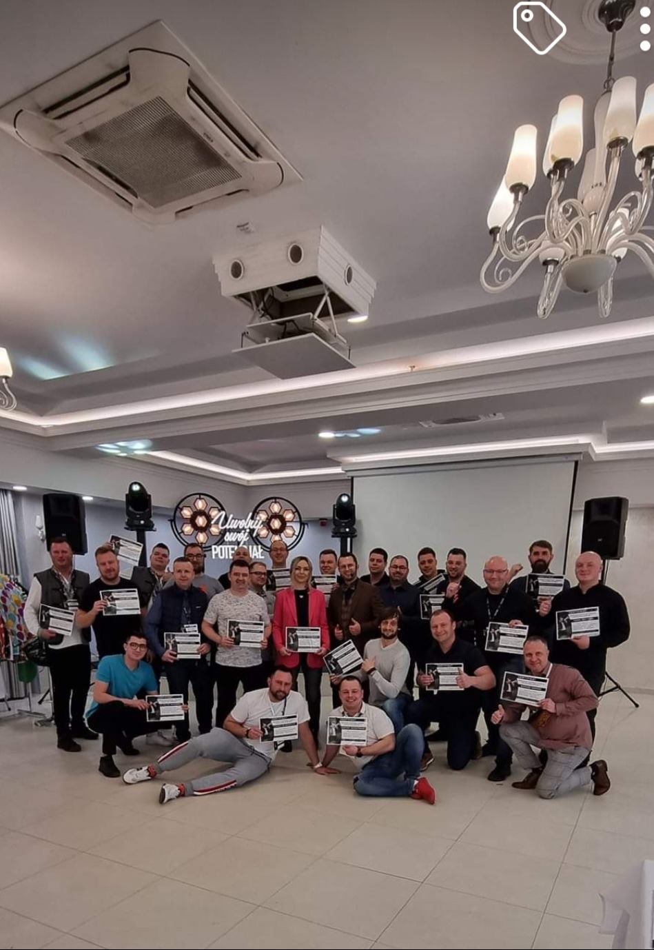 Grupa osób pozuje z dyplomami na tle sceny oświetlonej reflektorami, w tle widoczny napis 'Uwolnij swój potencjał'.