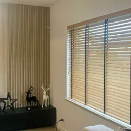 Jasne drewniane żaluzje poziome z czarnymi sznurkami zamontowane w oknie, widoczne elementy dekoracyjne: gwiazdy i figurki jeleni na szafce pod telewizorem.