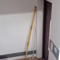 Wnętrze pokoju w trakcie remontu: poziomica oparta o ścianę, widoczne ślady po pracach na podłodze z terakoty i przy listwie przypodłogowej, częściowo widoczne drzwi.