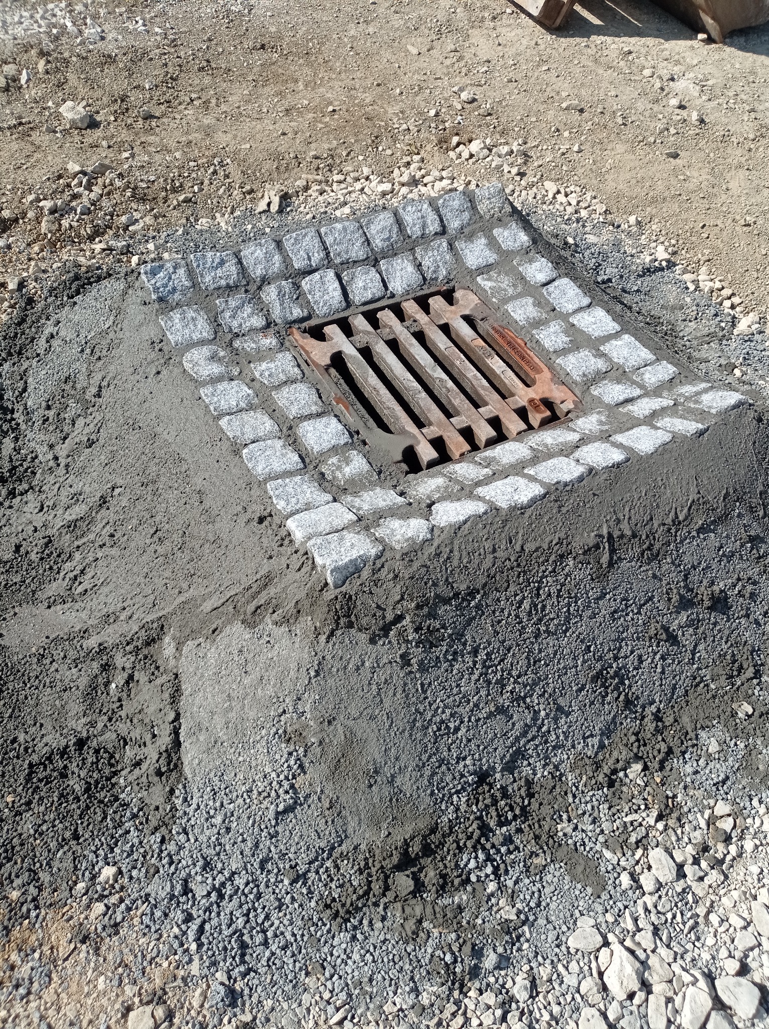 Montaż kratki ściekowej z obramowaniem z kostki granitowej, w trakcie prac ziemnych i betonowania, widoczne elementy rusztowania