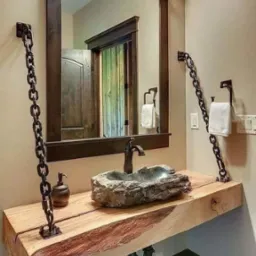 Unikalna łazienka z blatem z litego drewna podtrzymywanym przez łańcuchy, kamienna umywalka i lustro w ciemnej ramie.
