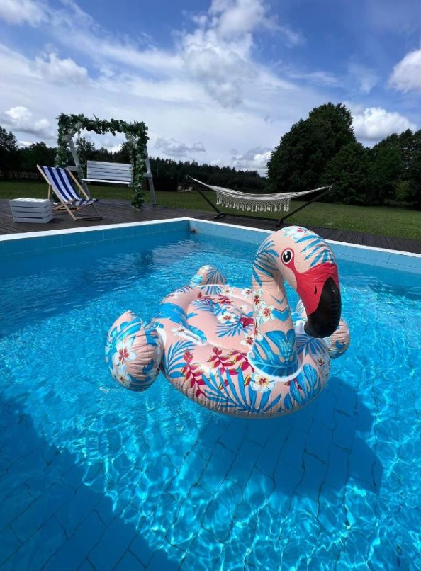 Nadmuchiwany flaming w basenie z turkusową wodą, w tle hamak i huśtawka ogrodowa.