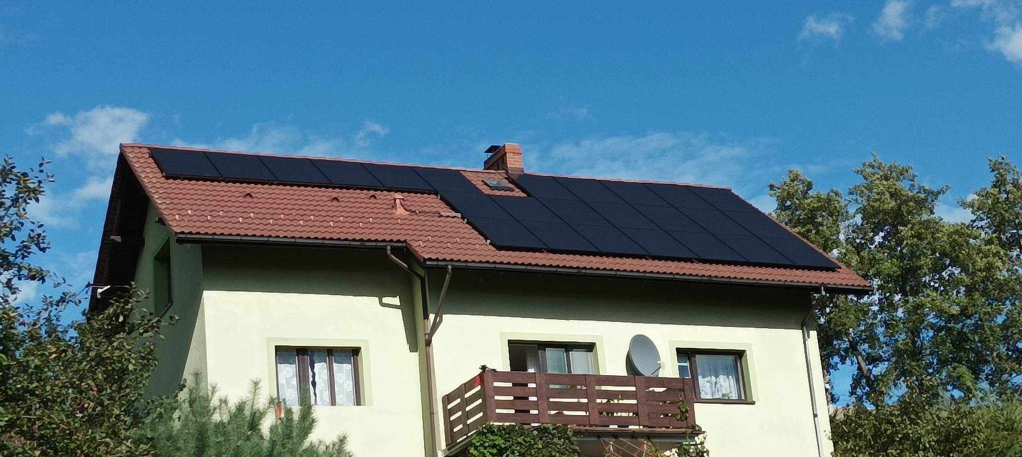 Dom jednorodzinny z panelami słonecznymi na dachu z czerwonej dachówki, widok z dołu na tle błękitnego nieba.