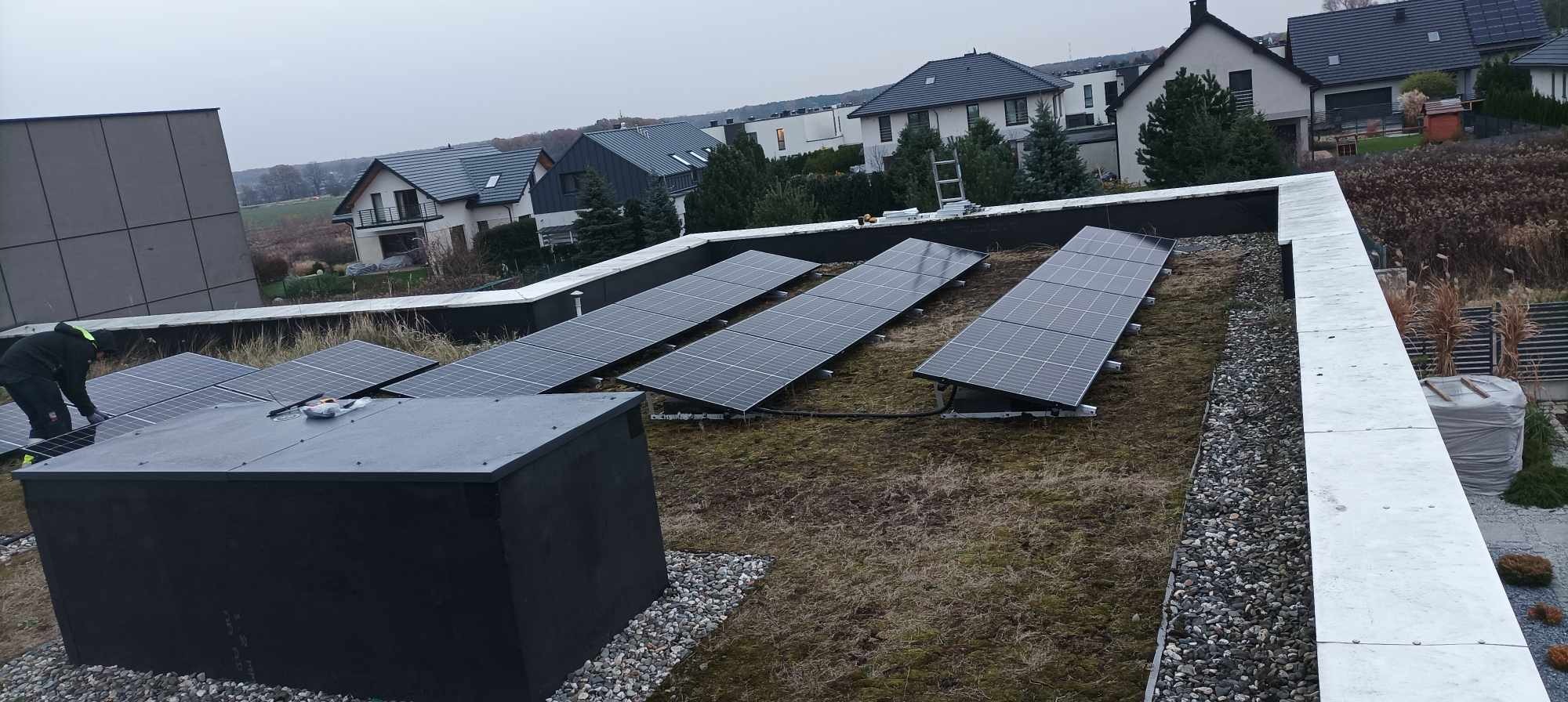 Instalacja paneli słonecznych na zielonym dachu budynku w Bytomiu. Widoczny pracownik w trakcie montażu, panele ułożone w rzędach, w tle zabudowa jednorodzinna.