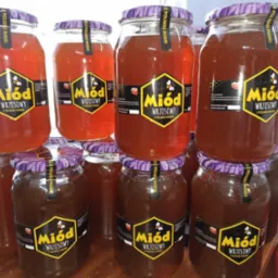 Słoiki z miodem wrzosowym ustawione w rzędach, widoczne etykiety z nazwą i logo producenta, różne odcienie miodu w słoikach.