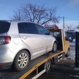 Srebrny samochód osobowy Volkswagen Touran na żółtej lawecie pomocy drogowej z włączonym pomarańczowym światłem ostrzegawczym, zimowy krajobraz w tle.