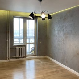 Serhii Melnyk - Pokój po odświeżeniu: parkiet, ściany z efektem betonu, biała listwa przypodłogowa, okno z grzejnikiem, designerska lampa sufitowa.