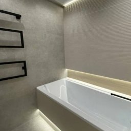 Serhii Melnyk - Nowoczesna łazienka z podświetlaną wanną, grzejnikiem drabinkowym i teksturowaną ścianą, oświetlona punktowo i listwą LED.