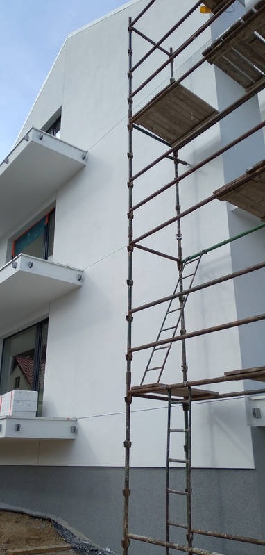 Ocieplanie ściany zewnętrznej budynku wielorodzinnego z balkonami, widoczne rusztowanie z drewnianymi podestami oraz drabina.