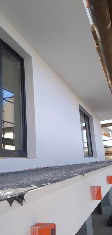 Świeżo pomalowana, biała ściana z oknami w czarnych ramach, widok z rusztowania zabezpieczonego pomarańczowymi elementami.