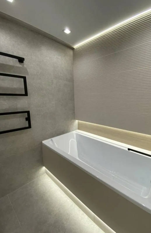 Nowoczesna łazienka z podświetlaną wanną, grzejnikiem drabinkowym i teksturowaną ścianą, oświetlona punktowo i listwą LED.