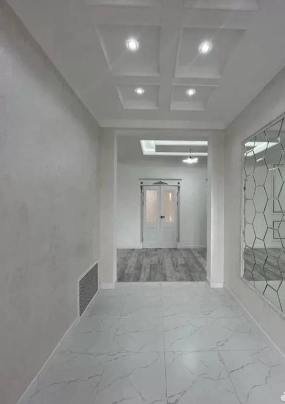 Nowoczesny korytarz z białymi ścianami o fakturze, marmurową podłogą, lustrem o geometrycznym wzorze i kwadratowymi lampami w suficie podwieszanym