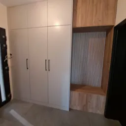 Nowoczesna szafa w przedpokoju z białymi frontami i drewnianym akcentem w postaci siedziska z pionowymi listwami dekoracyjnymi.