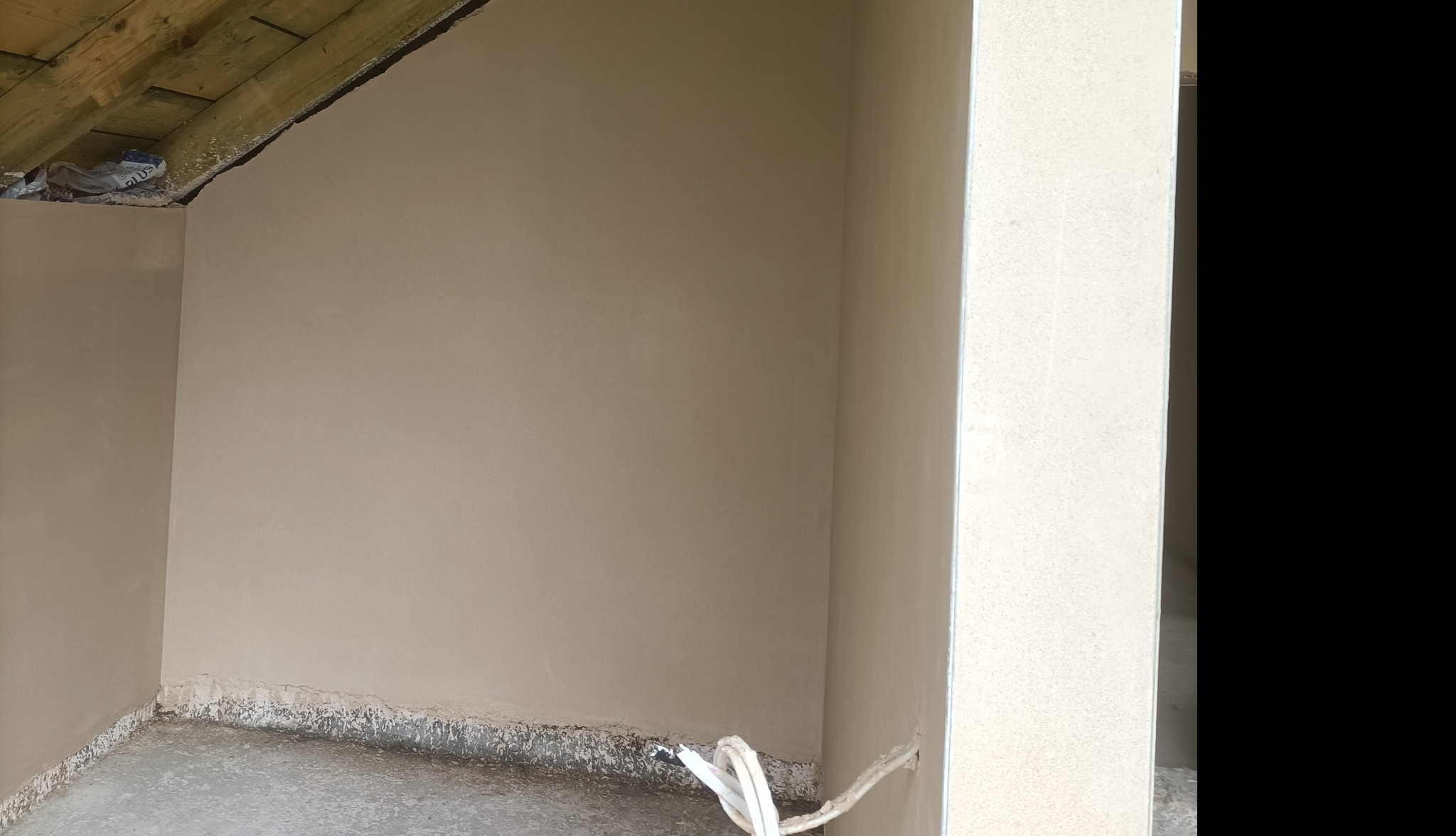 Świeżo otynkowane poddasze ze skośnym sufitem, widoczne kable elektryczne przy podłodze.