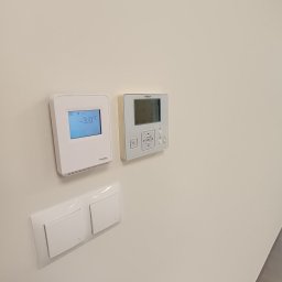 Łukasz Osowiecki Usługi Elektryczne - Białe panele sterowania klimatyzacją Hitachi i Schneider oraz włącznik światła na kremowej ścianie. Widoczna niska temperatura na wyświetlaczu.