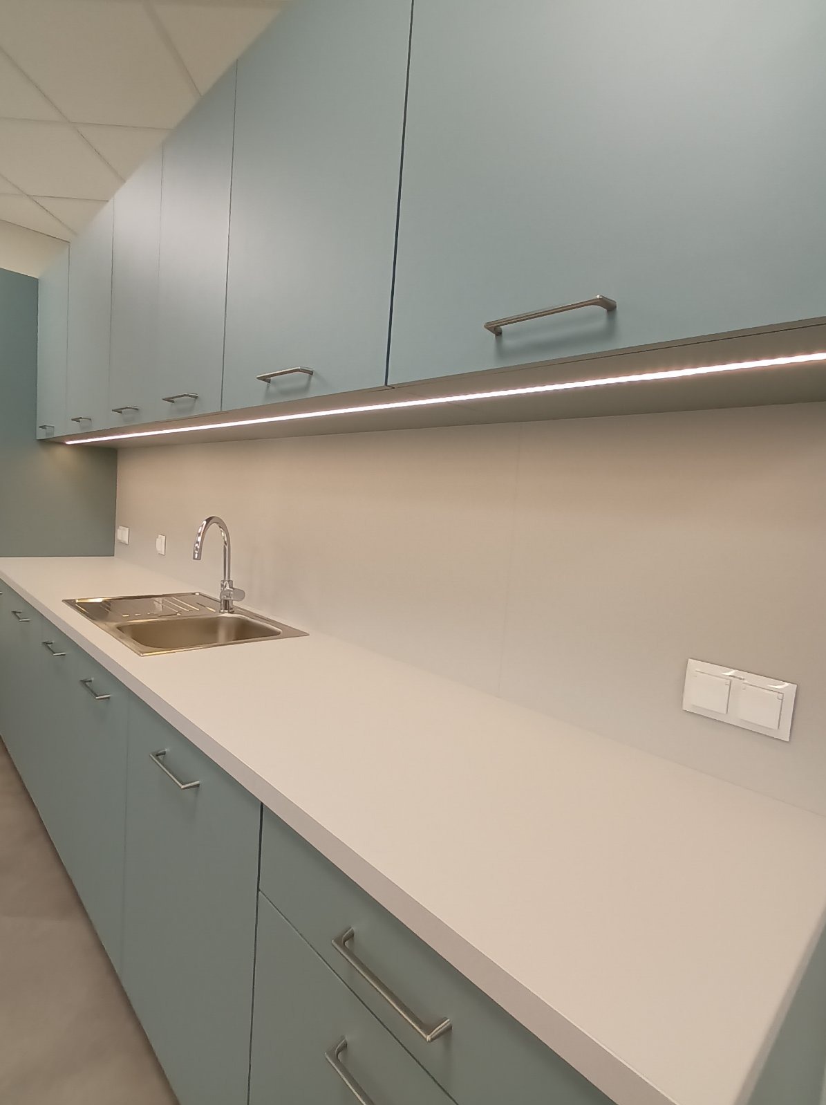 Błękitne szafki kuchenne z oświetleniem LED podszafkowym i chromowaną armaturą. Gniazdko elektryczne na ścianie. Nowoczesny design.