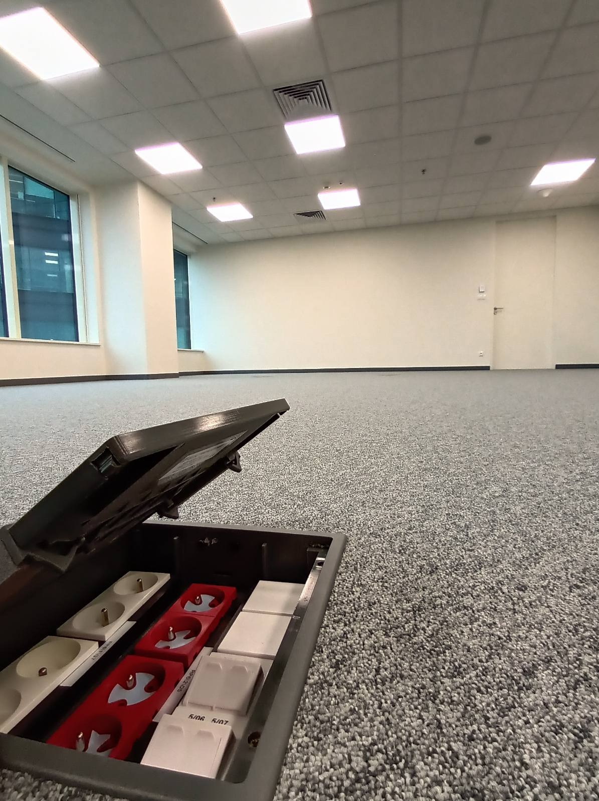 Otwarta podłogowa puszka elektryczna z gniazdami w nowym biurze, widok z bliska, szary dywan w tle. Widoczne gniazda zasilające i gniazda sieciowe.