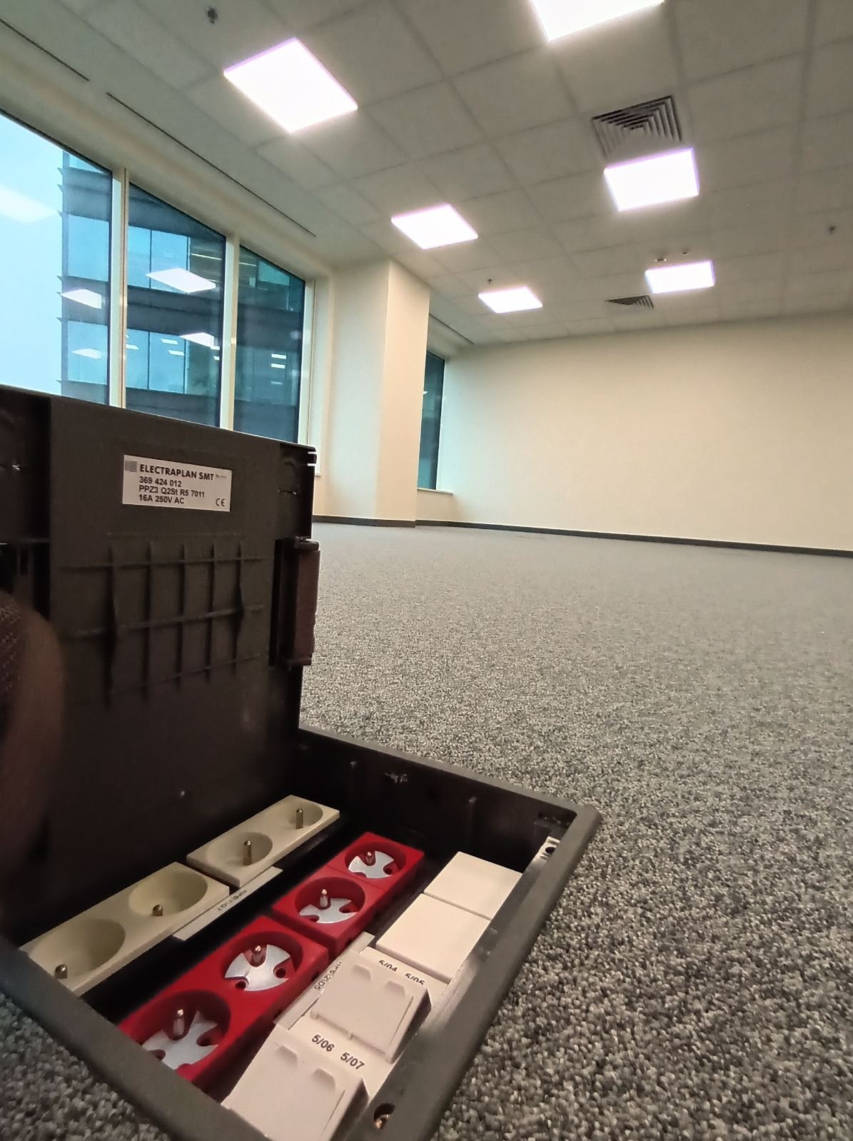 Otwarta podłogowa puszka elektryczna z gniazdami i wyłącznikami w nowym biurze z oknami. Widoczne detale producenta Electraplan SMT.