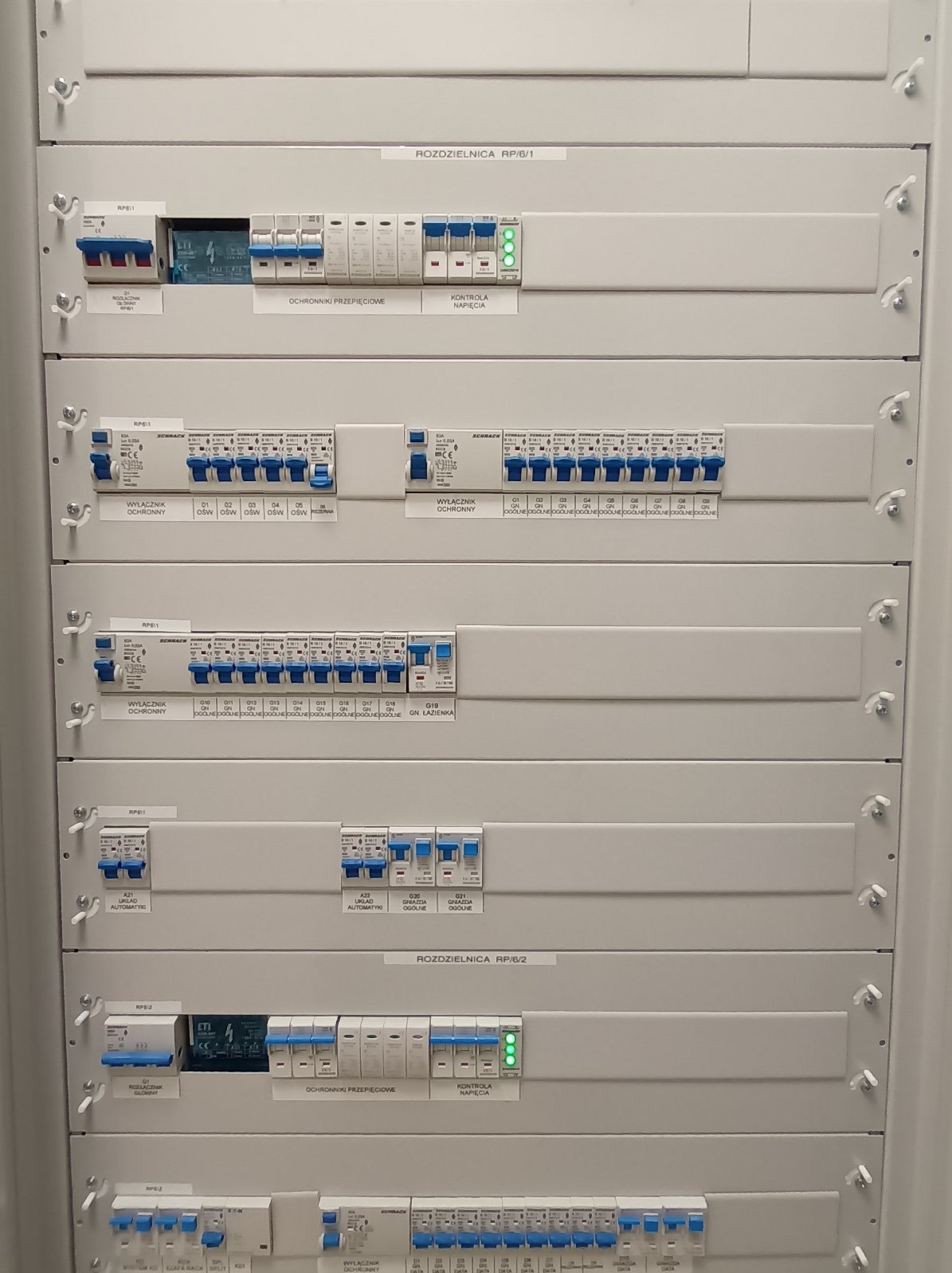 Szczegółowe ujęcie rozdzielnicy elektrycznej z wyłącznikami, bezpiecznikami i oznaczeniami, prezentujące instalację wewnątrz szafy sterowniczej. Widoczne elementy zabezpieczeń.