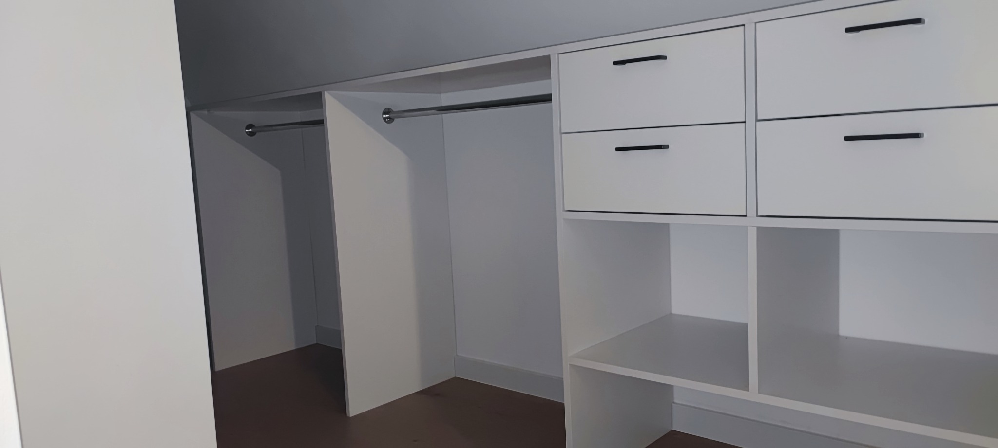 Biała szafa wnękowa z półkami i szufladami, widok wnętrza z drążkami na ubrania, minimalistyczne czarne uchwyty szuflad.