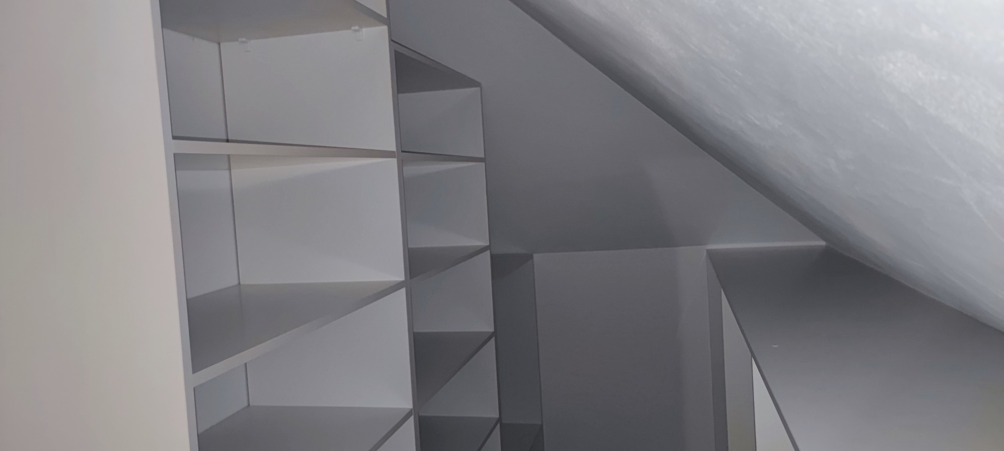 Wnętrze szafy wnękowej z białymi półkami, dopasowanej do skosu poddasza, widok z boku.