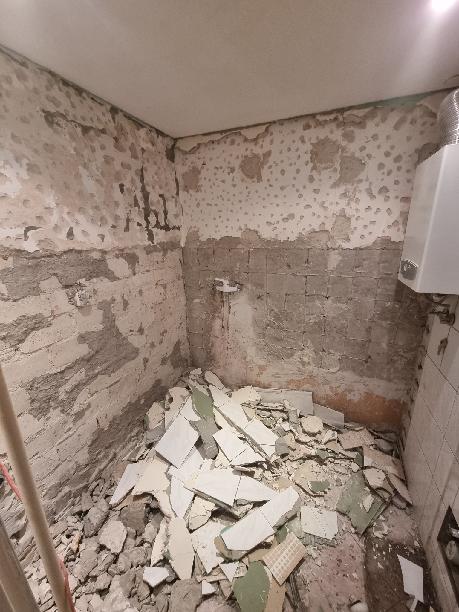 Demontaż płytek w łazience, widoczne fragmenty usuniętych płytek i resztki zaprawy na ścianach, przygotowanie do prac remontowych.