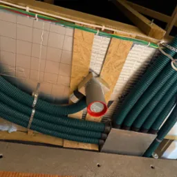 Zielone rury wentylacyjne rekuperacji zamontowane pod sufitem, widoczne elementy instalacji i izolacji. Ujęcie z dołu, podkreślające złożoność systemu.