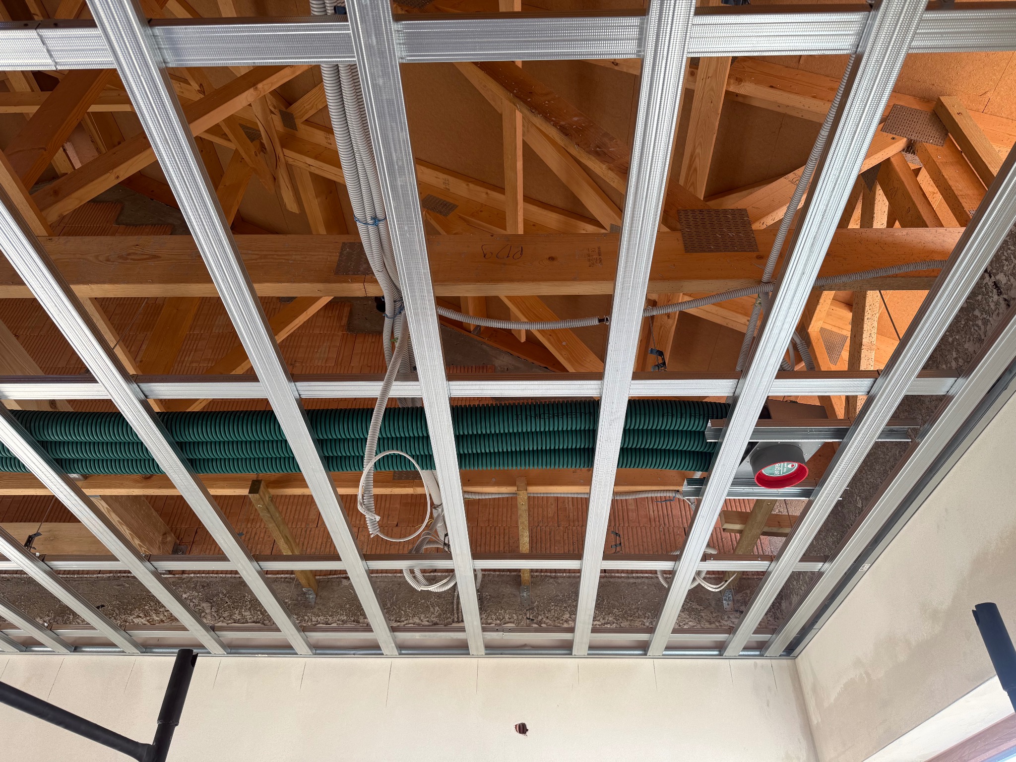 Montaż sufitu podwieszanego z widoczną konstrukcją metalową, instalacją elektryczną i wentylacyjną. Widok z dołu, surowe wykończenie.