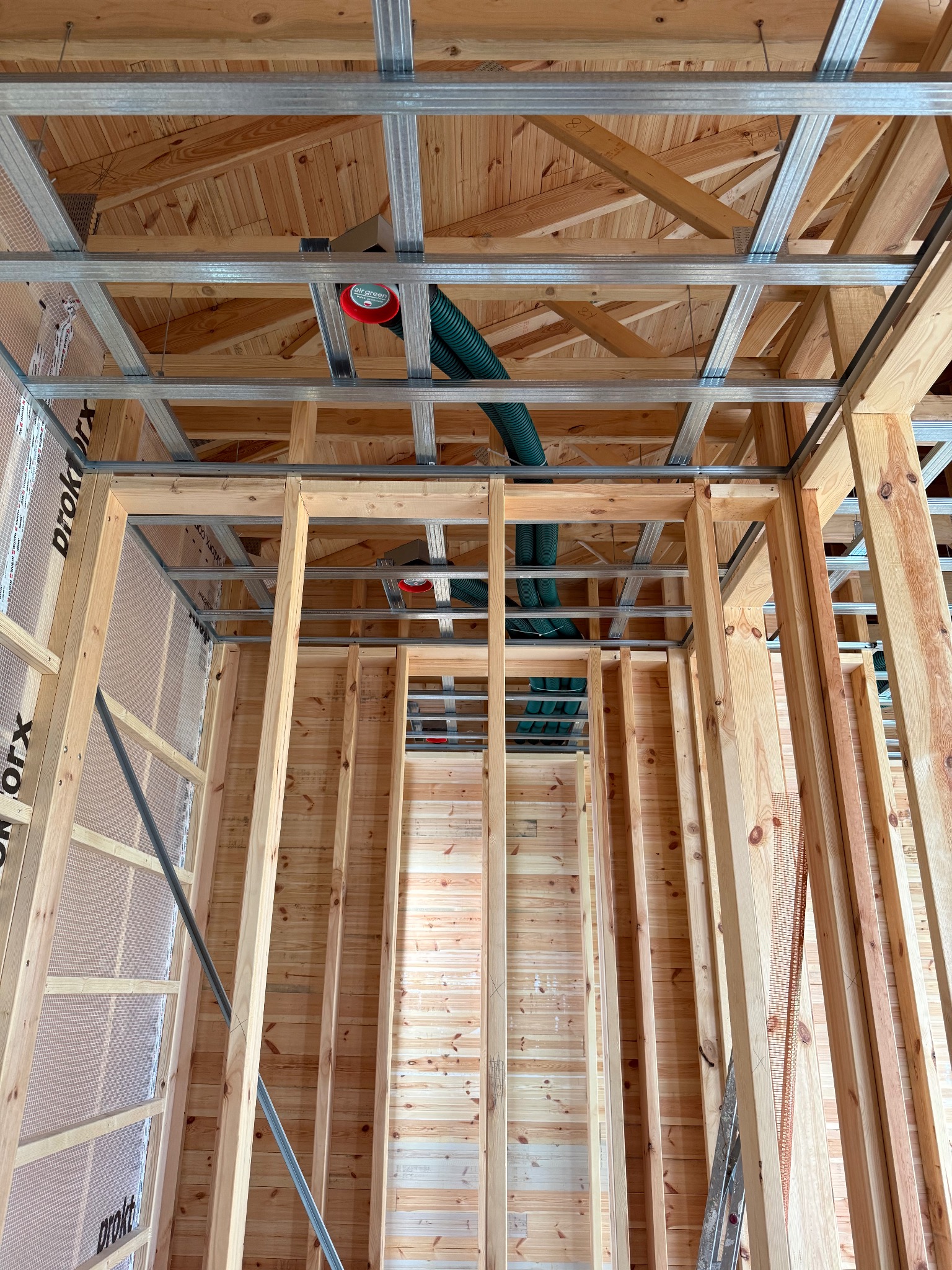Montaż rekuperacji w Koszalinie: Widok na drewnianą konstrukcję ścian i sufitu z elementami instalacji wentylacyjnej, zielone rury i metalowe profile.