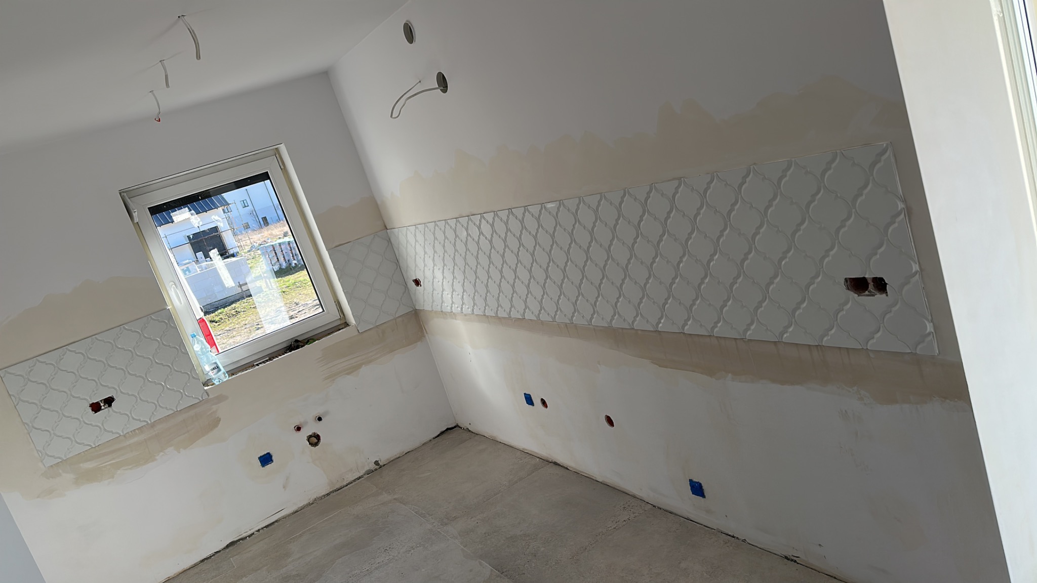 Wnętrze łazienki w trakcie montażu dekoracyjnych płytek ściennych o wzorze marokańskim, widoczne wystające kable, przygotowane otwory na gniazdka elektryczne, oraz częściowo wykończona podłoga...