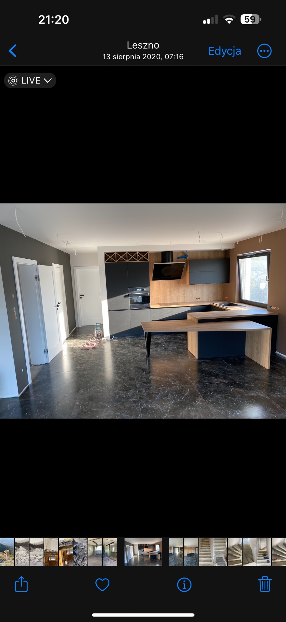 Ciemna podłoga z płytek imitujących marmur w nowocześnie wykończonej kuchni z czarnymi szafkami i drewnianym blatem, widoczne niedokończone prace elektryczne.