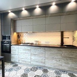 METER DECOR VADYM TYMOSEVYCH - Nowoczesna kuchnia z szarymi szafkami górnymi i dolnymi z efektem drewna, czarnym blatem, białymi płytkami ściennymi typu metro i heksagonalną mozaiką na podłodze i ścianie po prawej stronie.