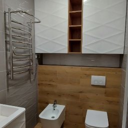 METER DECOR VADYM TYMOSEVYCH - Nowoczesna łazienka z drewnopodobnymi płytkami, białą armaturą i szafkami z geometrycznym wzorem na ścianie, grzejnik drabinkowy.