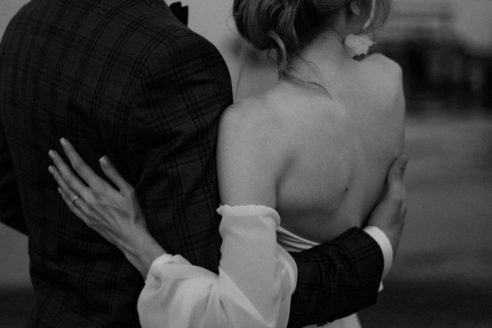 Czarno-białe ujęcie obejmującej się pary młodej, z widocznym pierścionkiem na palcu kobiety i wzorzystą marynarką mężczyzny.