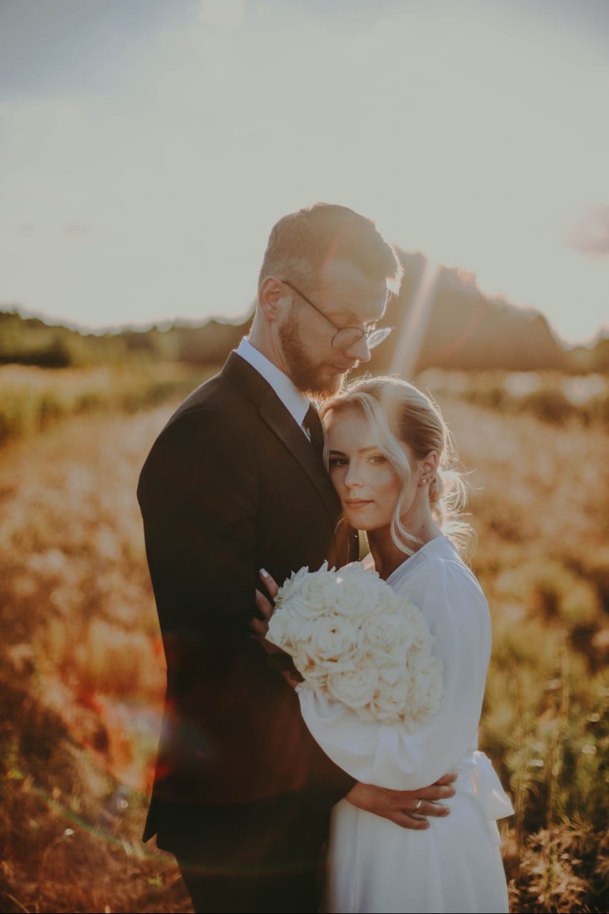 Para młoda w Niedrzwicy Dużej podczas sesji w plenerze, panna młoda trzyma bukiet białych róż, w tle zachodzące słońce.