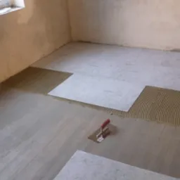 Podłoże pod płytki z naniesionym klejem i częściowo ułożonymi płytami Sopro, widoczna kielnia z czerwoną rączką.