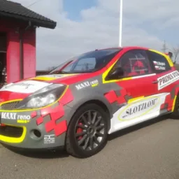 Renault Clio w barwach rajdowych z naklejonymi logotypami sponsorów, widok z boku na tle garażu.