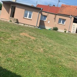 Usługi Budowlane Jakub Jedynak - Niski dom z beżową elewacją, czerwonym dachem i białymi oknami, widziany z trawnika w słoneczny dzień.